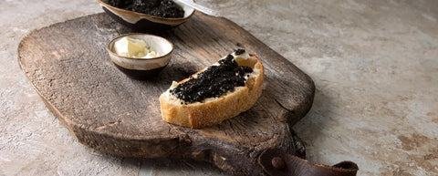 buttered slice bread topped with caviar on a wooden board next to bowls of butter and caviar