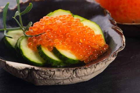 a bowl of sliced cucumbers topped with salmon caviar