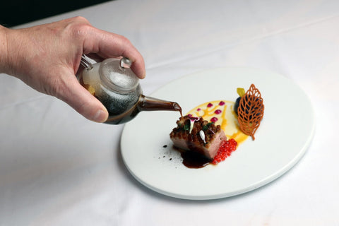 chef drizzling sauce over a caviar topped duck breast on a plate