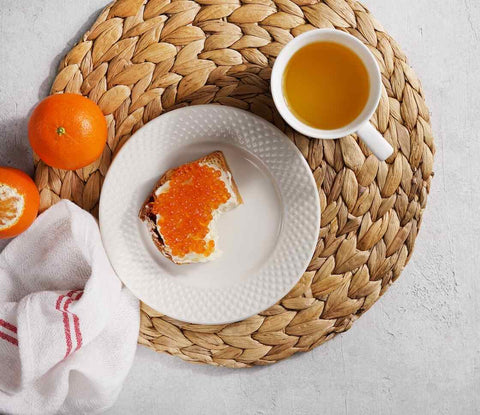 cup of green tea and a cream caviar topped toast on a plate next to tangerines