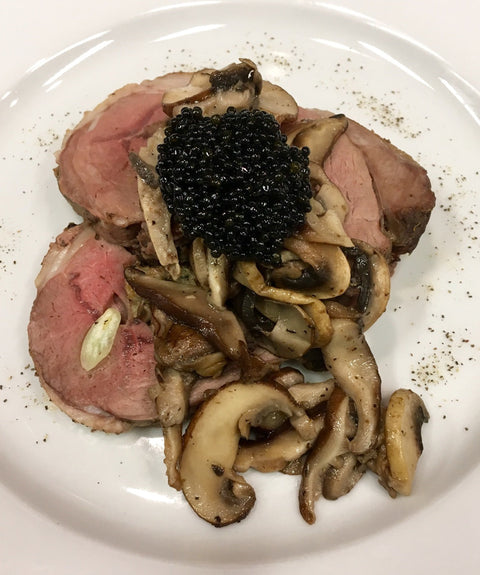 Leg of Lamb with Mushrooms and Hackleback Caviar on a white plate