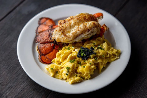 scrambled eggs topped with caviar plated next to a lobster tail