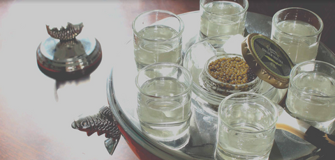 glasses of clear liquid on a platter with an open jar of caviar