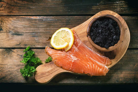 smoked salmon, bowl of caviar, a lemon slice on a wooden board