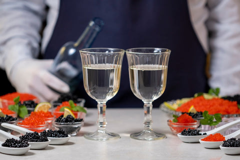 waiter holding a bottle, standing in front of 2 full glasses and caviar servings