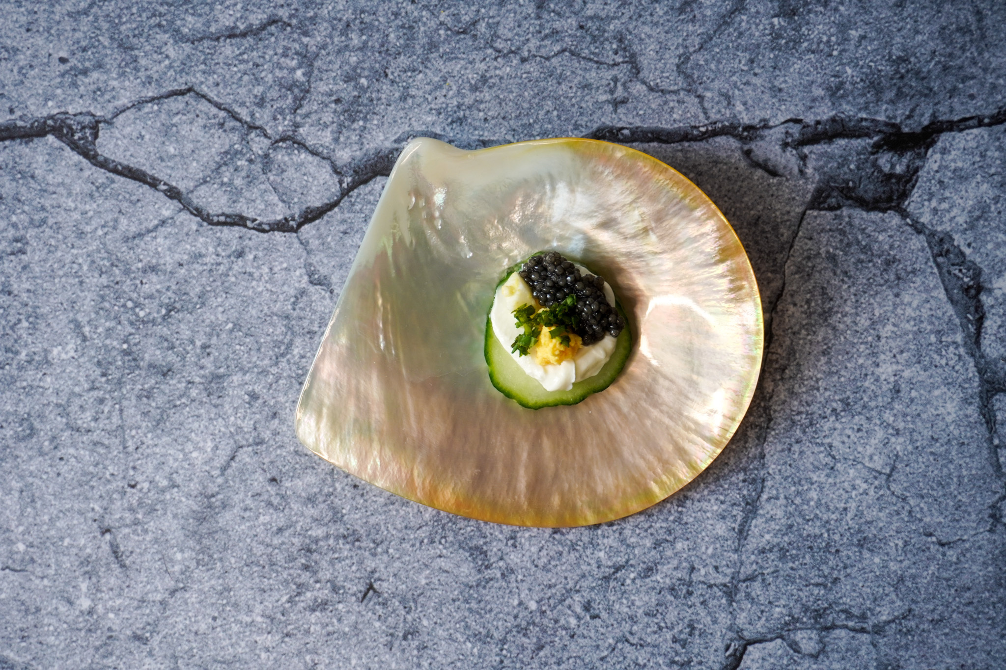 Black caviar, creme fraiche, and chives on a cucumber plated on a shell